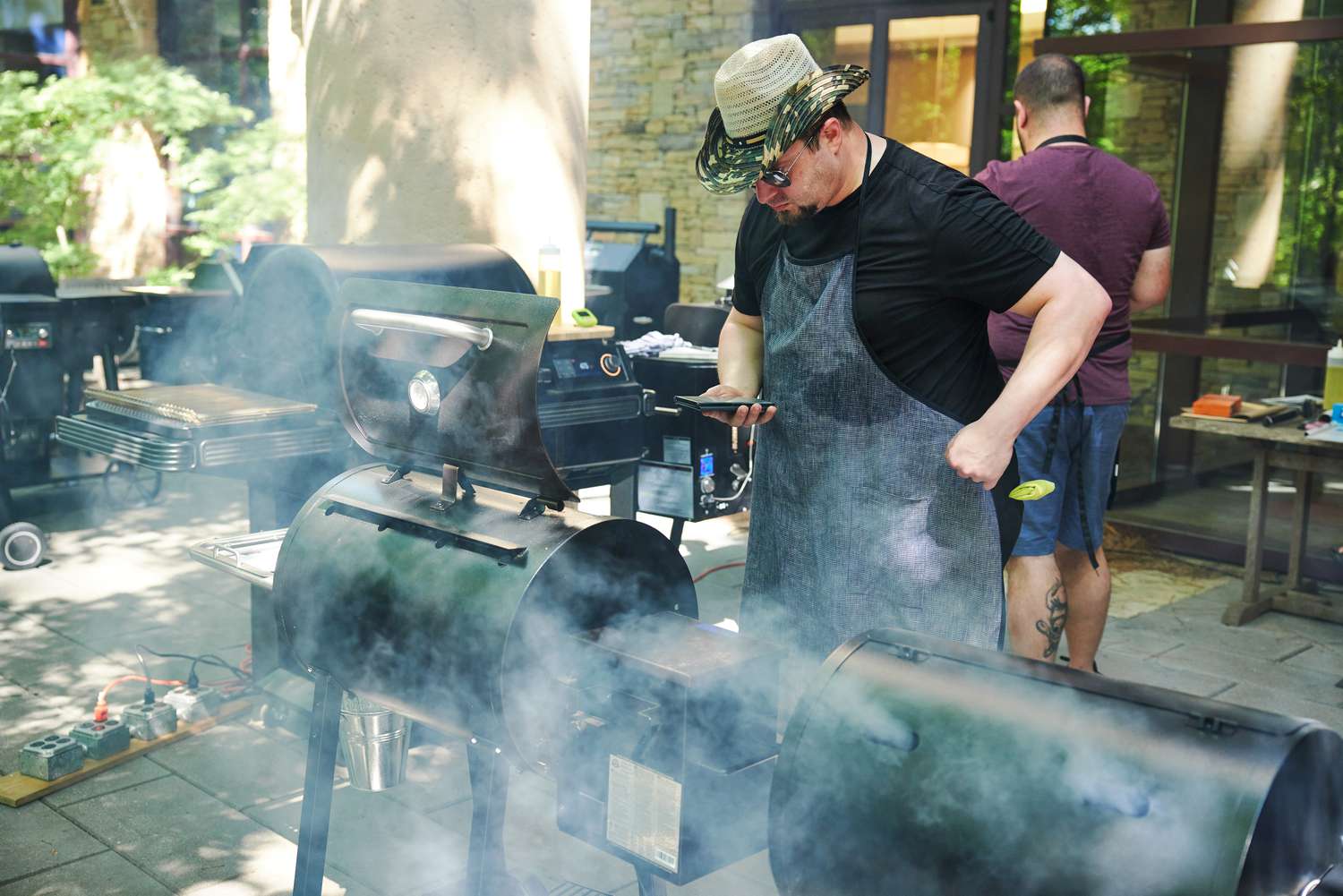 Person looking at phone while standing in front of a Pit Boss 440 Deluxe Wood Pellet Grill with several other grills nearby