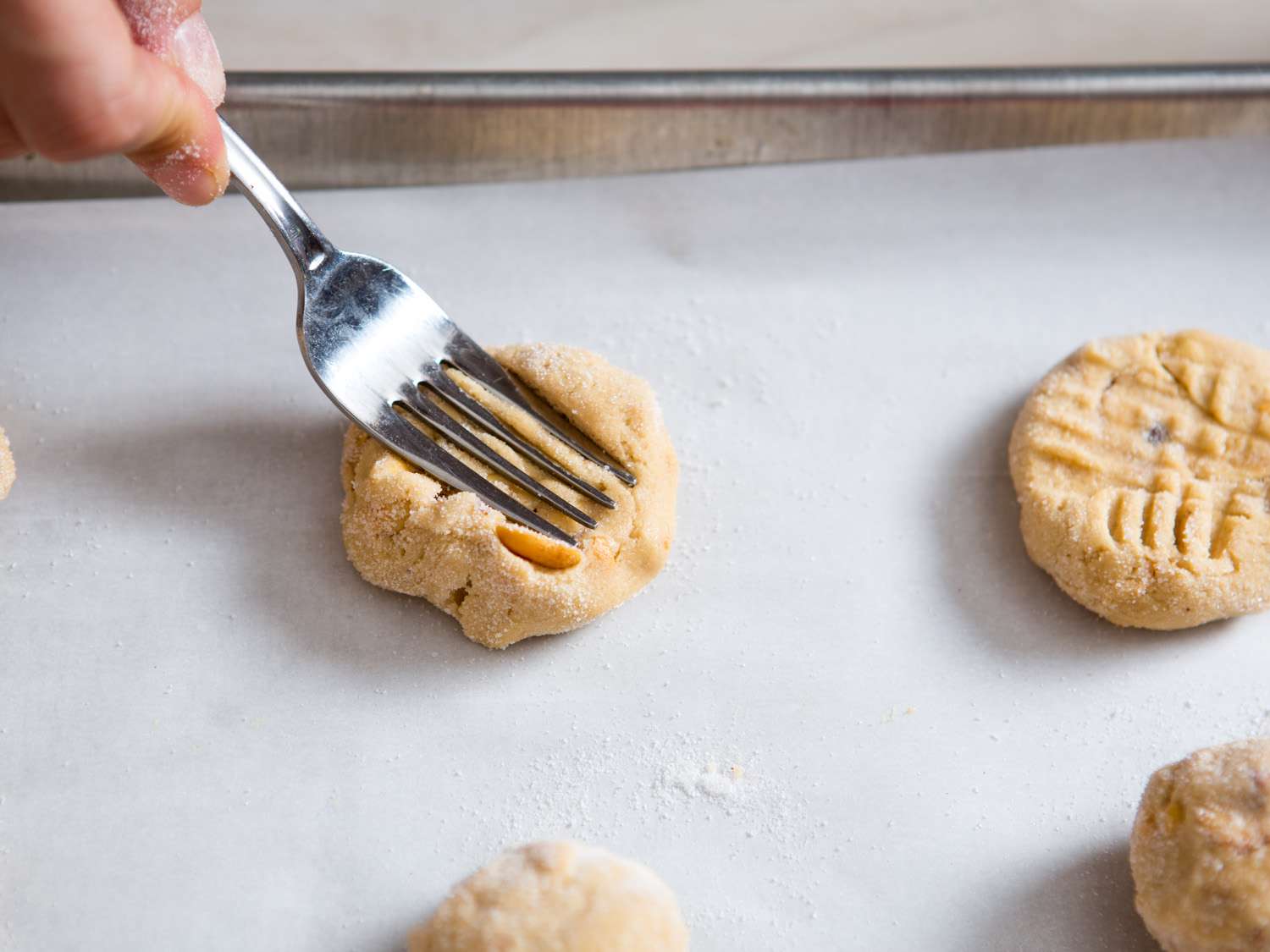 Author pressing crisscross pattern into balls of raw cookie dough arranged on a parchment-lined baking sheet.