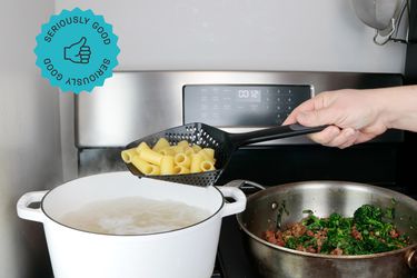 A colander spoon holding drained rigatoni of a Dutch oven full of boiling water