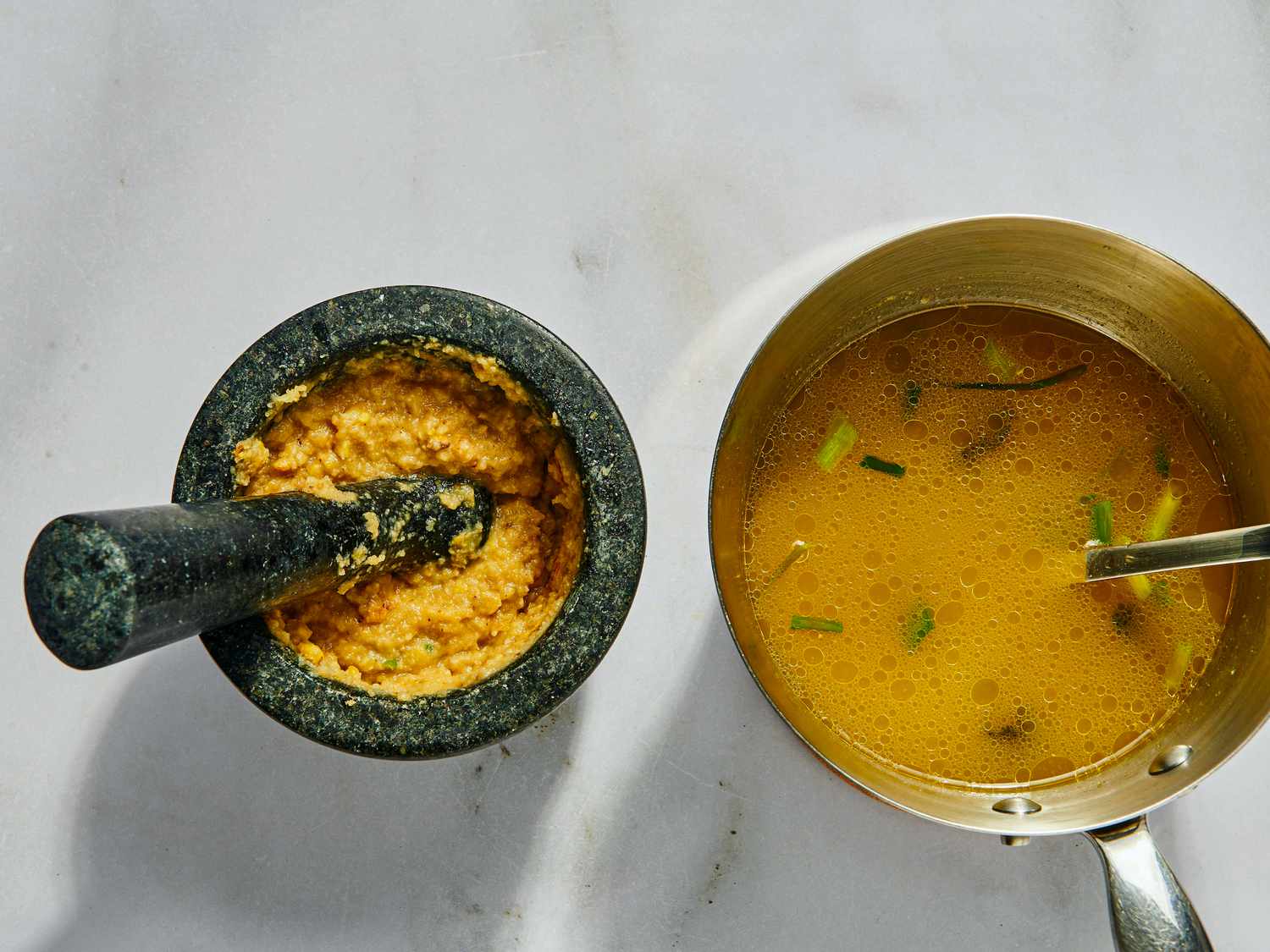 garlic, pork rinds and salt grinding in a mortar and pestle with pot of broth next to it