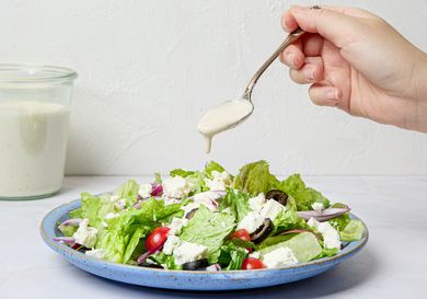 A spoon drizzling dressing onto a green salad with various toppings on a plate