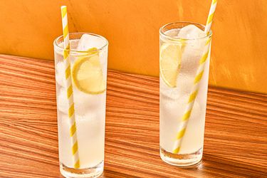 Two glasses of iced lemon drinks with striped straws on a wooden surface