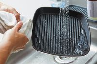 A person running the Cuisinart Chef's Classic 9.25-inch Square Grill Pan under water in a sink 