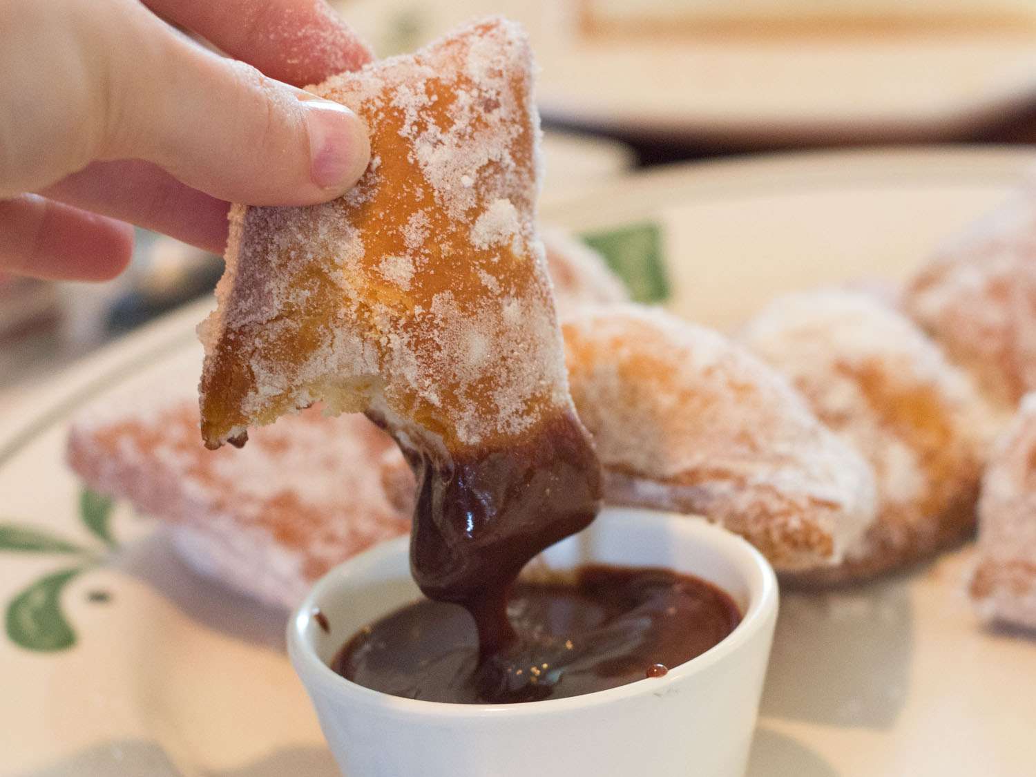 A Zeppoli being dipped into a chocolate sauce 