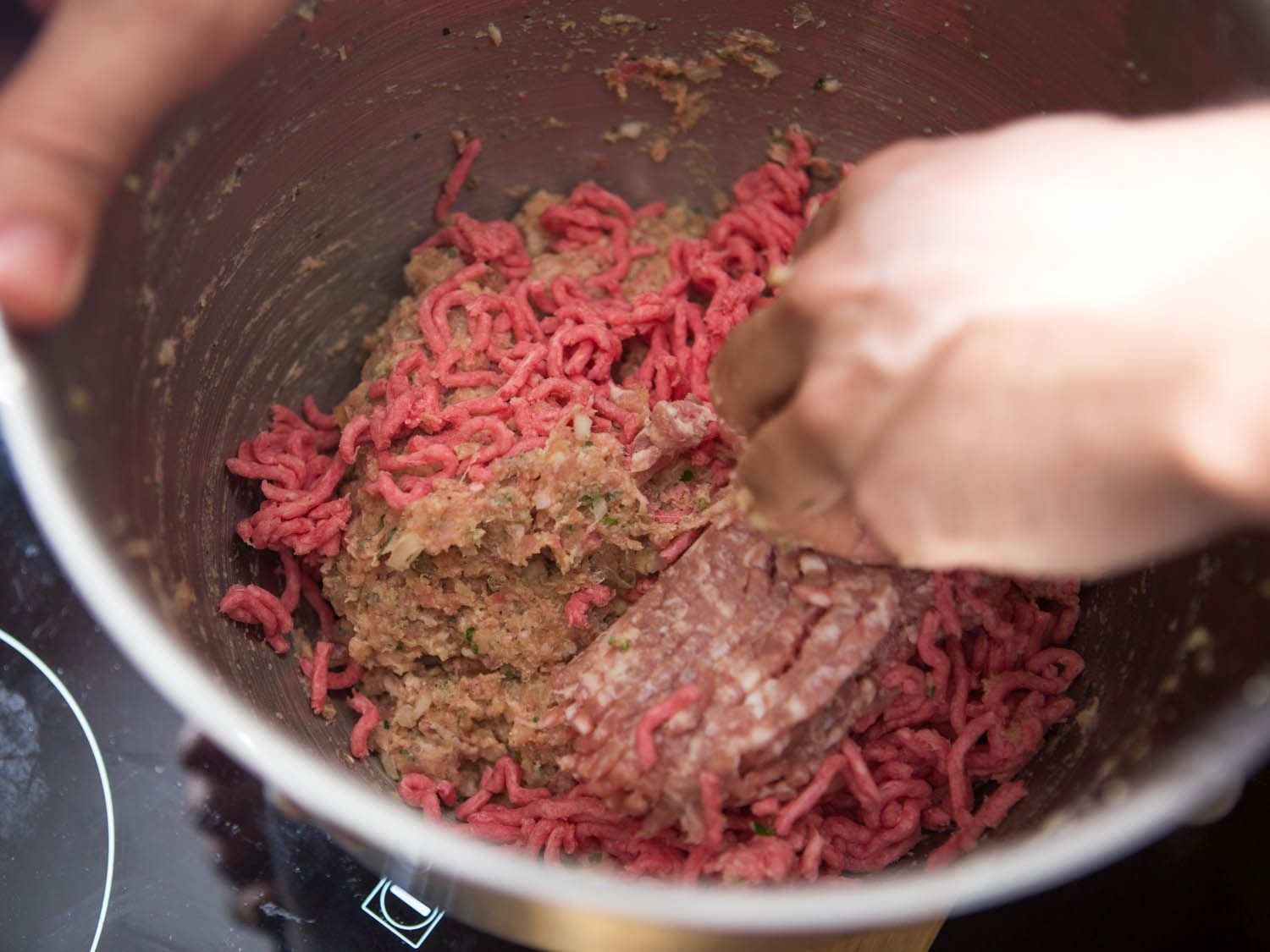 Using hands to mix in ground meat to emulsified meat and flavorings mixture for meatballs.