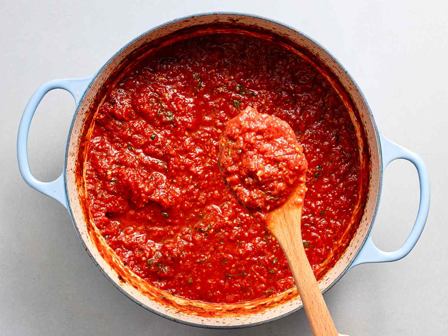 A spoon lifting some of the cooked tomato sauce out of a dutch oven to show its texture and color.
