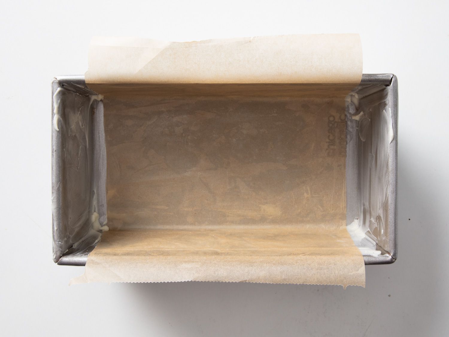 A buttered loaf pan with a piece of parchment tucked into it.