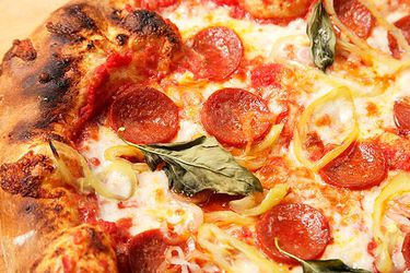 Closeup of pepperoni pizza topped with pickled banana peppers and basil leaves.