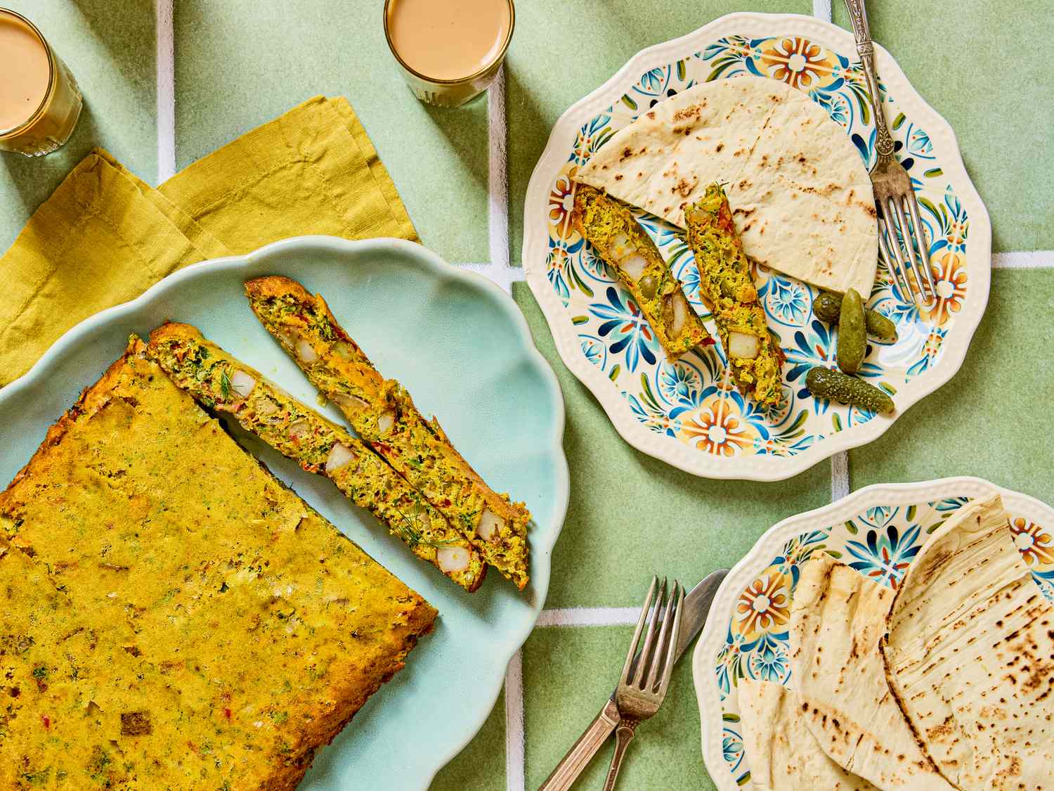 Three plates containing an assortment of baked goods and flatbreads accompanied by glasses of tea