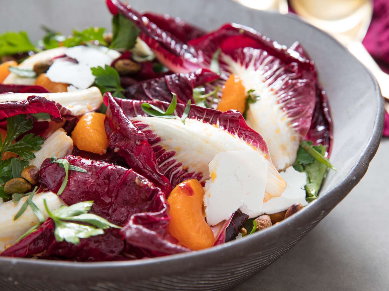 Close-up of a large ceramic salad bowl filled with dressed Trevisano radicchio, mandarin orange segments, herbs, pistachios, and ricotta salata.
