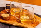 Two hot toddies served on a wooden board with lemon slices, next to a small bowl of demerara sugar