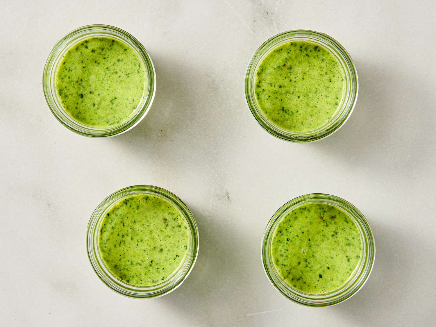 Four jars of green kale and mushroom egg mixture on a light surface prepared for cooking