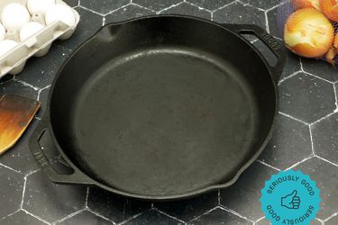 the lodge dual handled skillet on a black tile surface with a carton of eggs to the left and a bag of yellow onions on the right