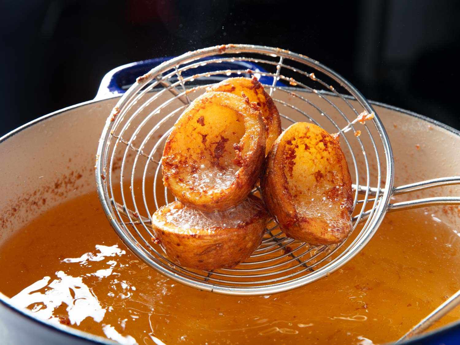 Potato skin cups being lifted out of the fryer once golden and crispy.