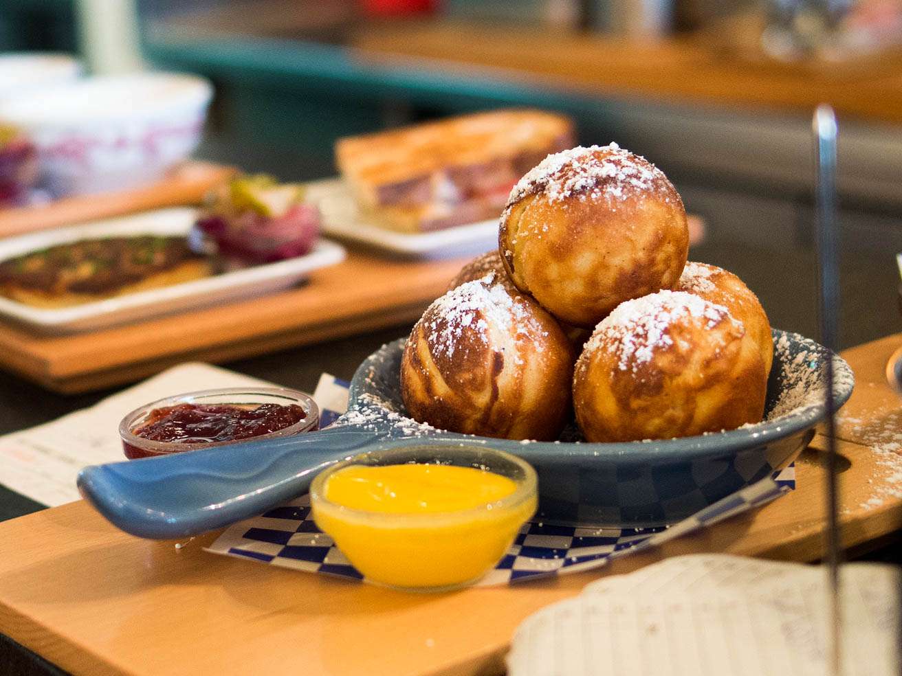 A small dish with ebleskiver that are sprinkled with powdered sugar. Two small bowls of jam are next to them.