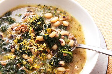 Close up view of a sausage and kale soup with peas. 