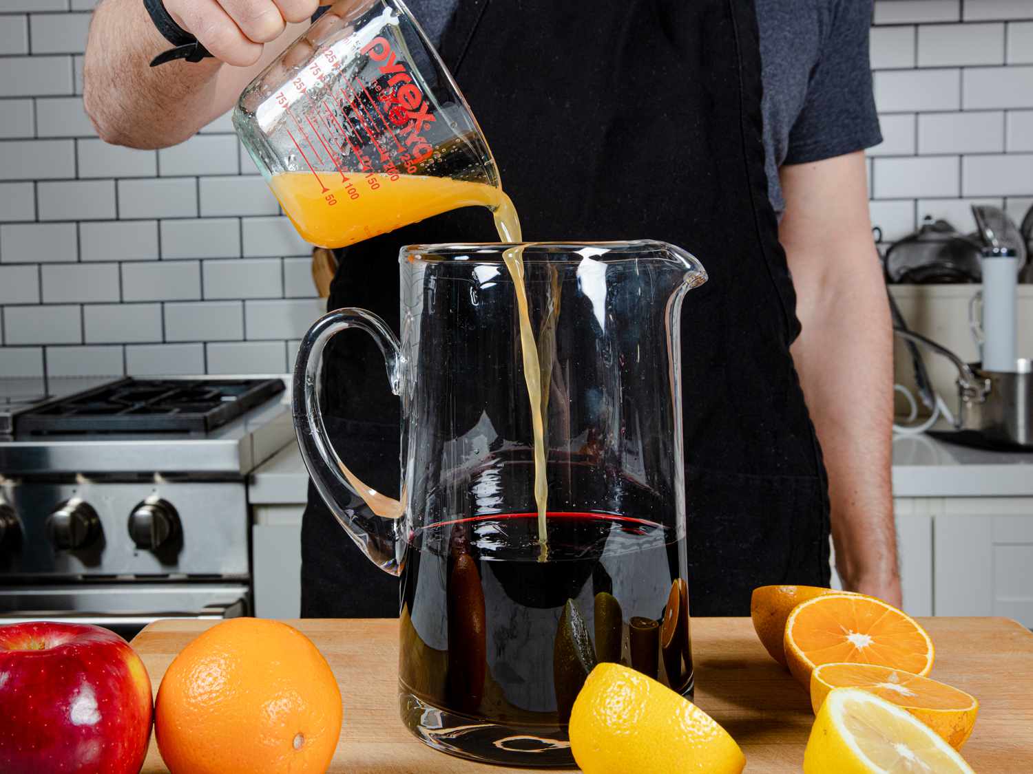 Red wine, liquor, and citrus juices are combined in a large pitcher by the author.