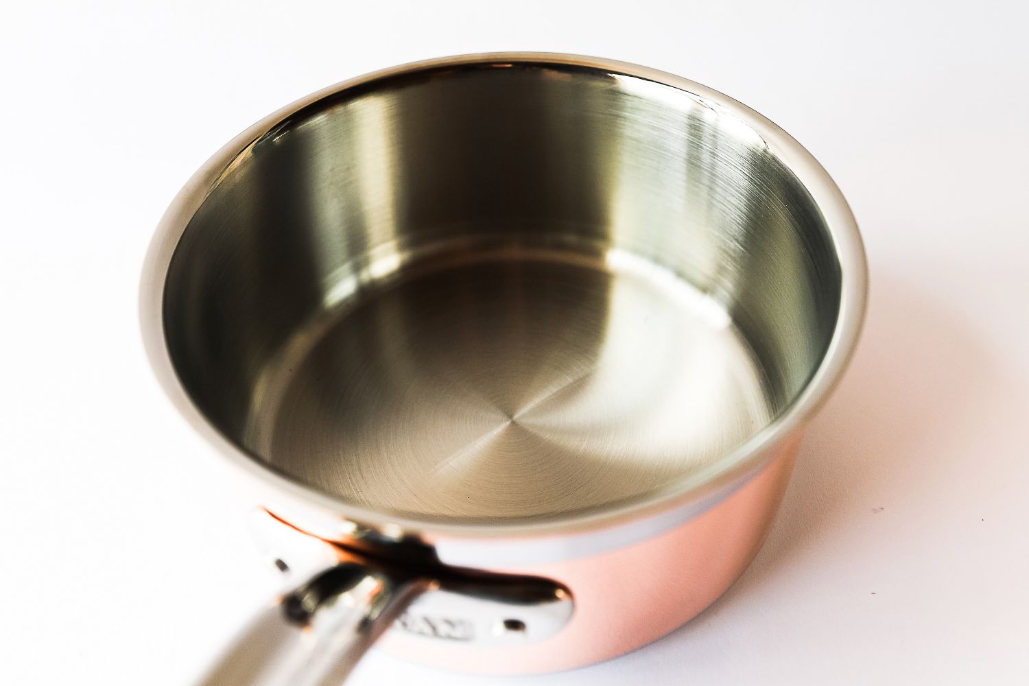A stainless steel pot with a copper outer layer featuring a reflective interior and metallic handle