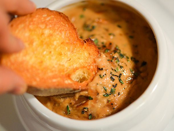 Dipping a piece of toasted bread into a small bowl of French onion dip.