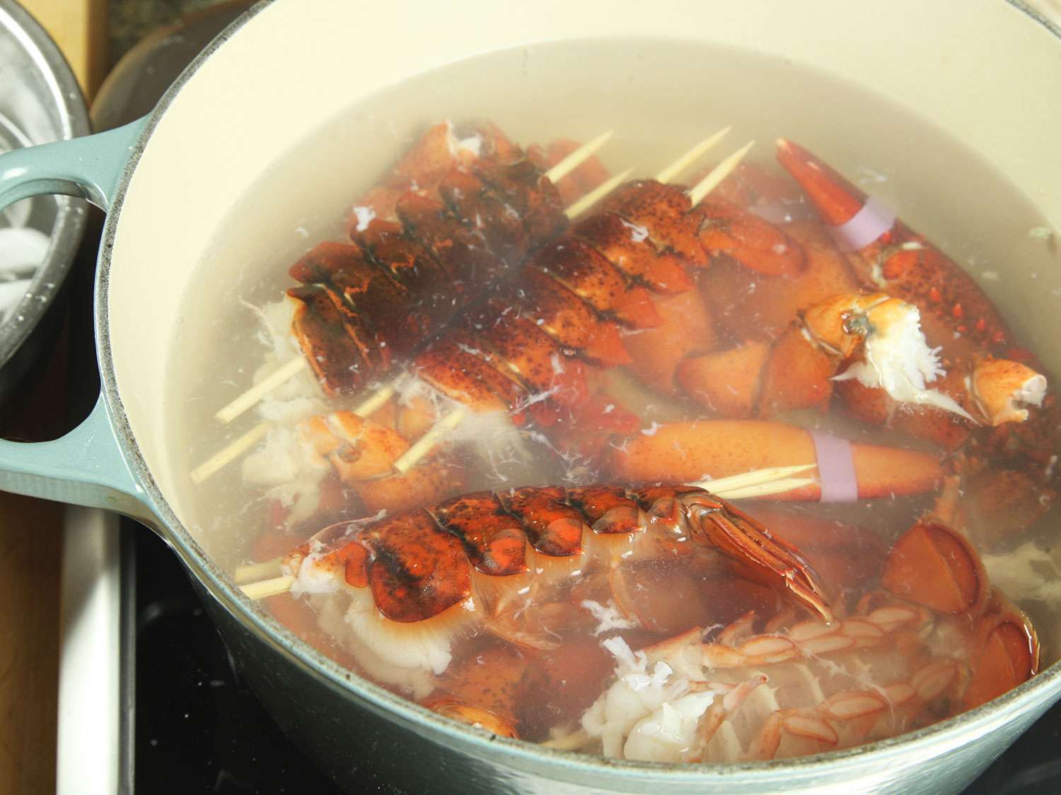 Straightened lobster tails cooking briefly in a Dutch oven of boiling water.