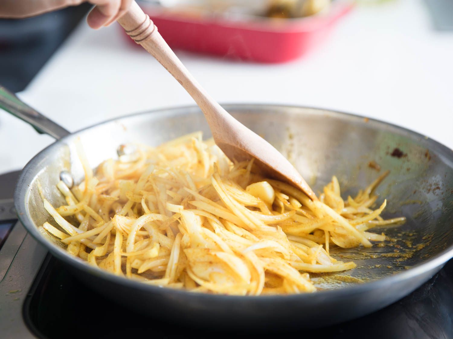 Sliced onions being fried in a stainless steel pan.
