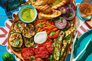 An assortment of grilled vegetables including zucchini, eggplant, onions, and tomatoes, served with bread and dips on a platter