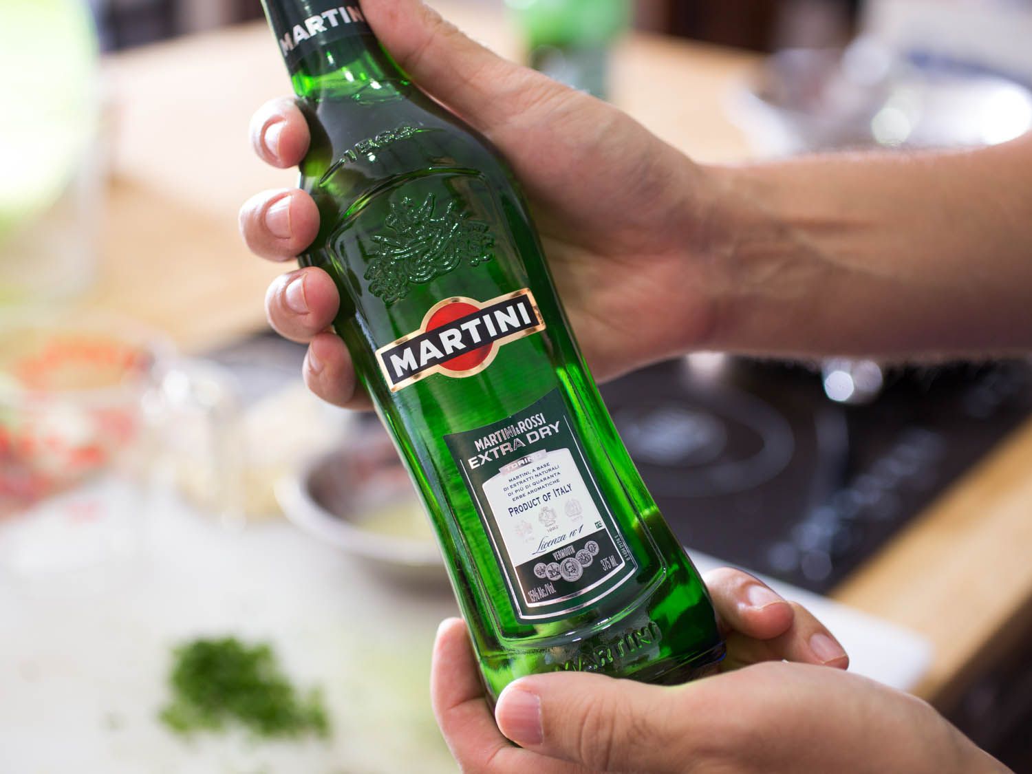 A hand holding up a green bottle of Martini & Rossi extra-dry vermouth.