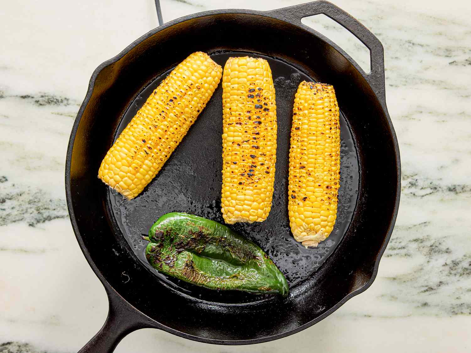 A skillet containing roasted corn on the cob and a poblano pepper