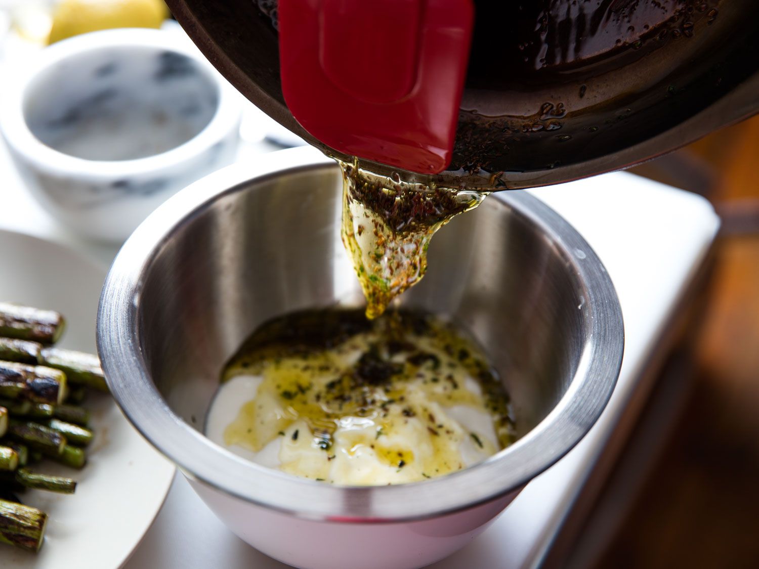 The hot caraway and thyme oil being poured into a metal bowl holding yogurt.