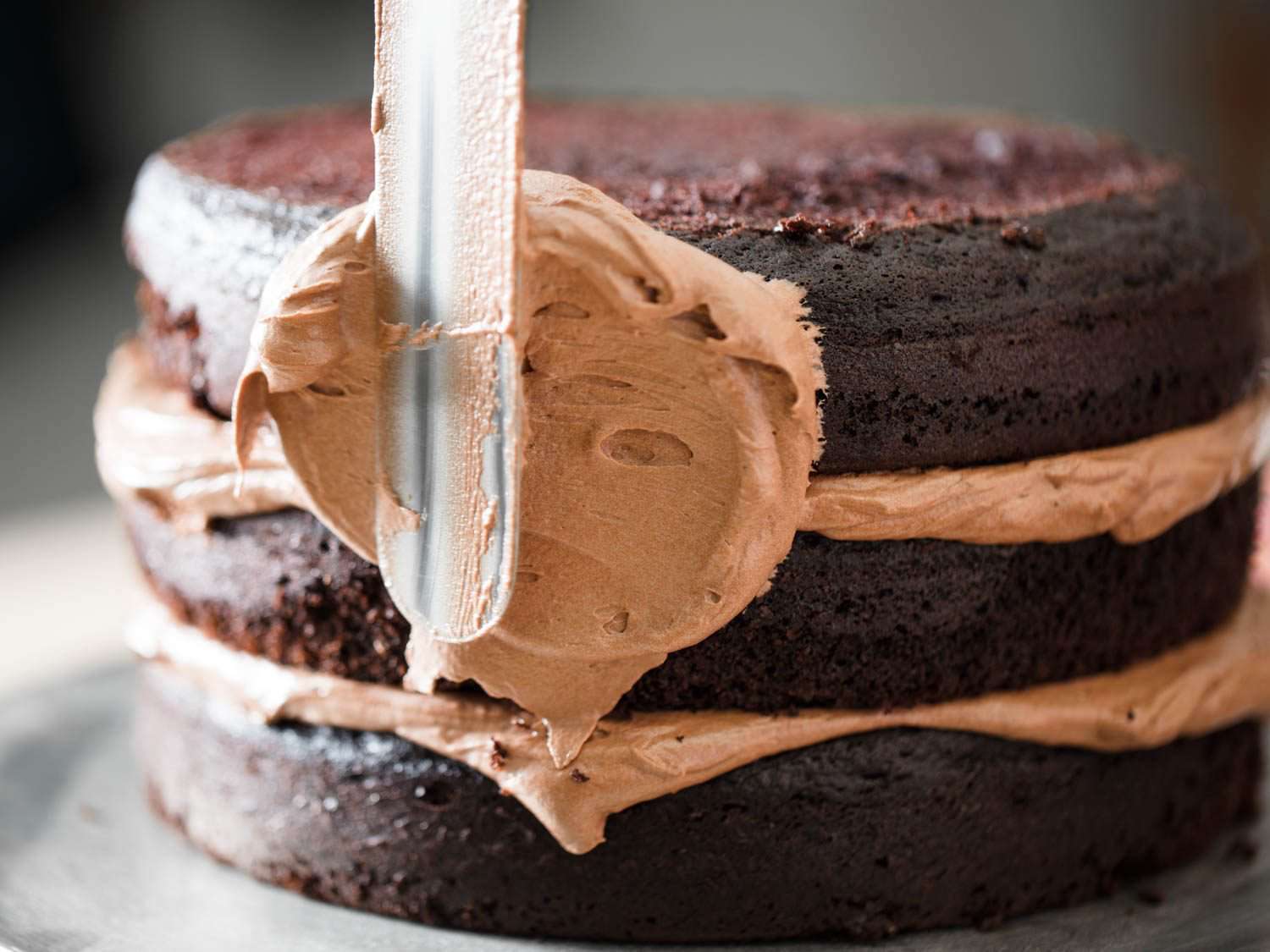 Frosting sides of three-layer Devil's food cake with chocolate Swiss buttercream.