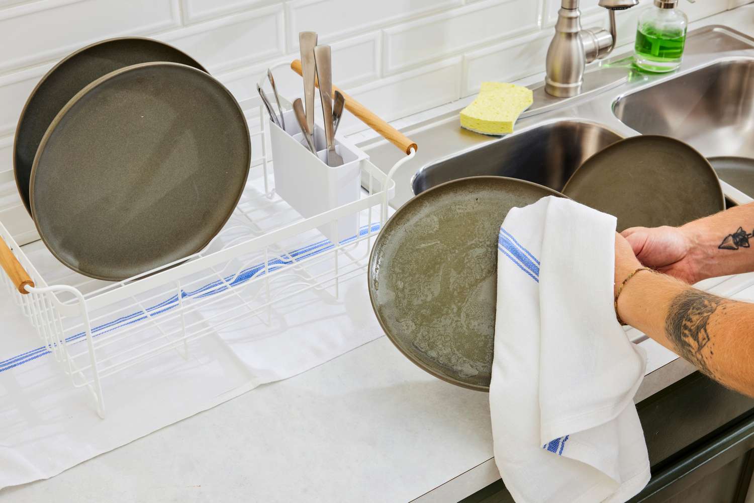 A person drying plates with a blue and white striped towel