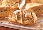 Maple scone being drizzled with glaze displayed on a cooling rack with other scones in the background