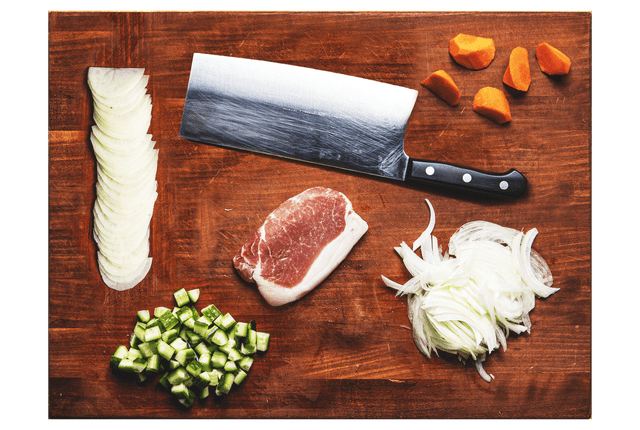 Overhead view of a cutting board with a knife and chopped vegetables and meat