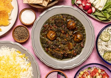 Overhead of Khoresh E Ghormeh Sabzi surrounded with rice, dips, and vegetables 