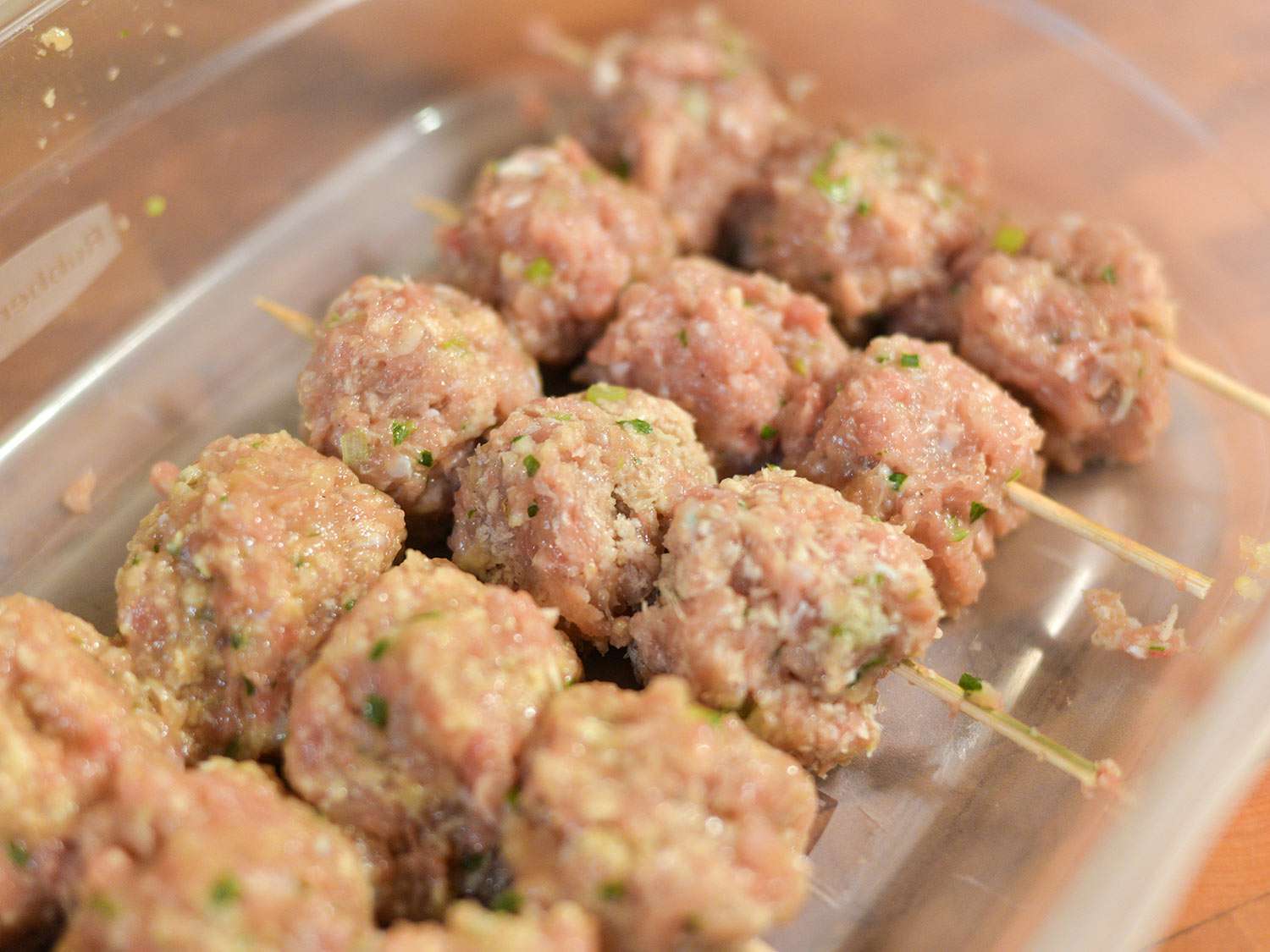 Raw Japanese chicken meatballs on small skewers in a glass dish. There are three meatballs on each skewer.