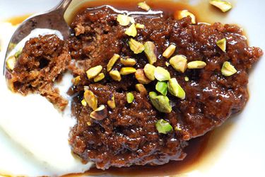Closeup of a serving of sticky toffee pudding, topped with chopped pistachios.