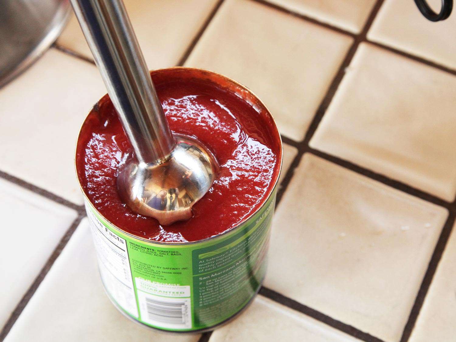 Author puréeing a can of whole tomatoes with an immersion blender.
