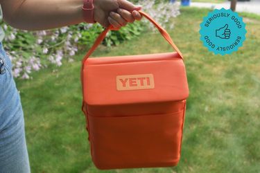 a person holding the handle on a bright orange yeti daytrip lunchbox 