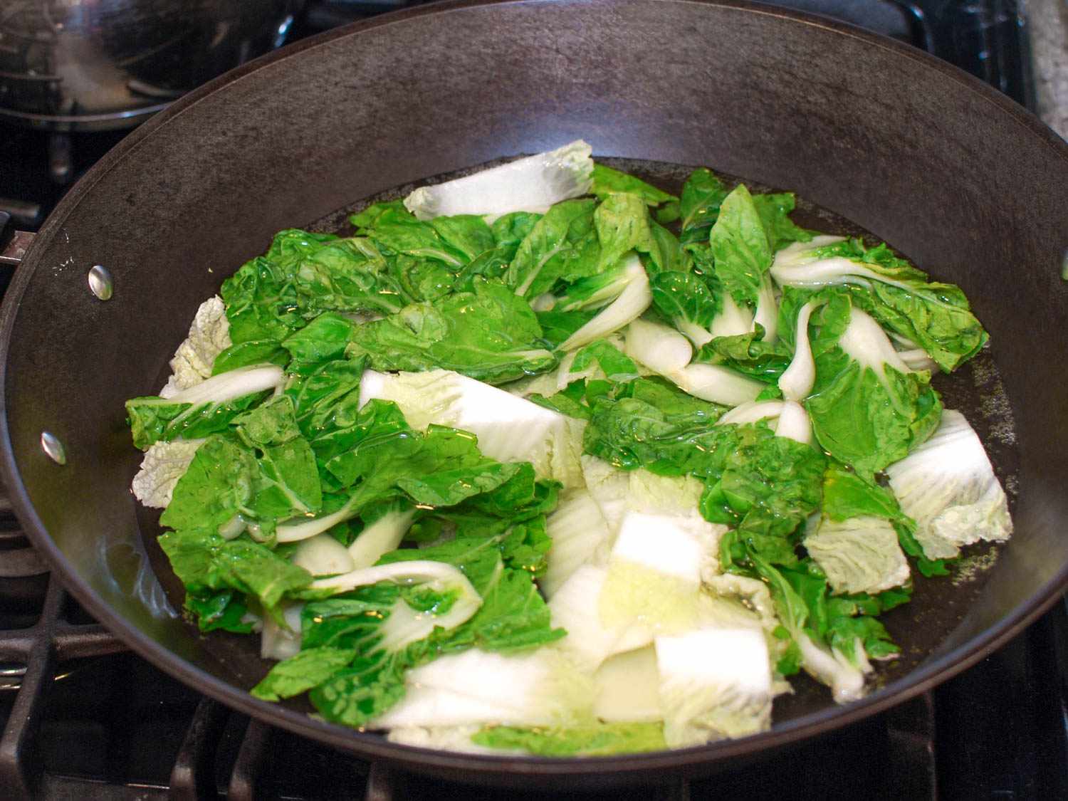 Baby bok choy and Napa cabbage cooking in a wok with salted water.