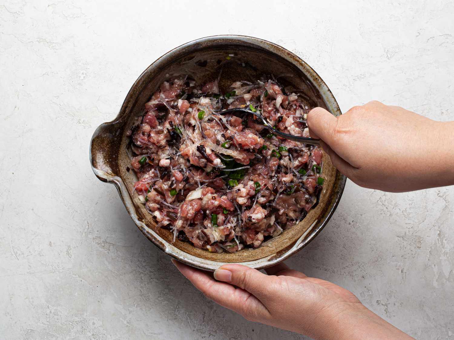 Overhead view of mixing pork, egg, noodles, and seasonings in a bowl