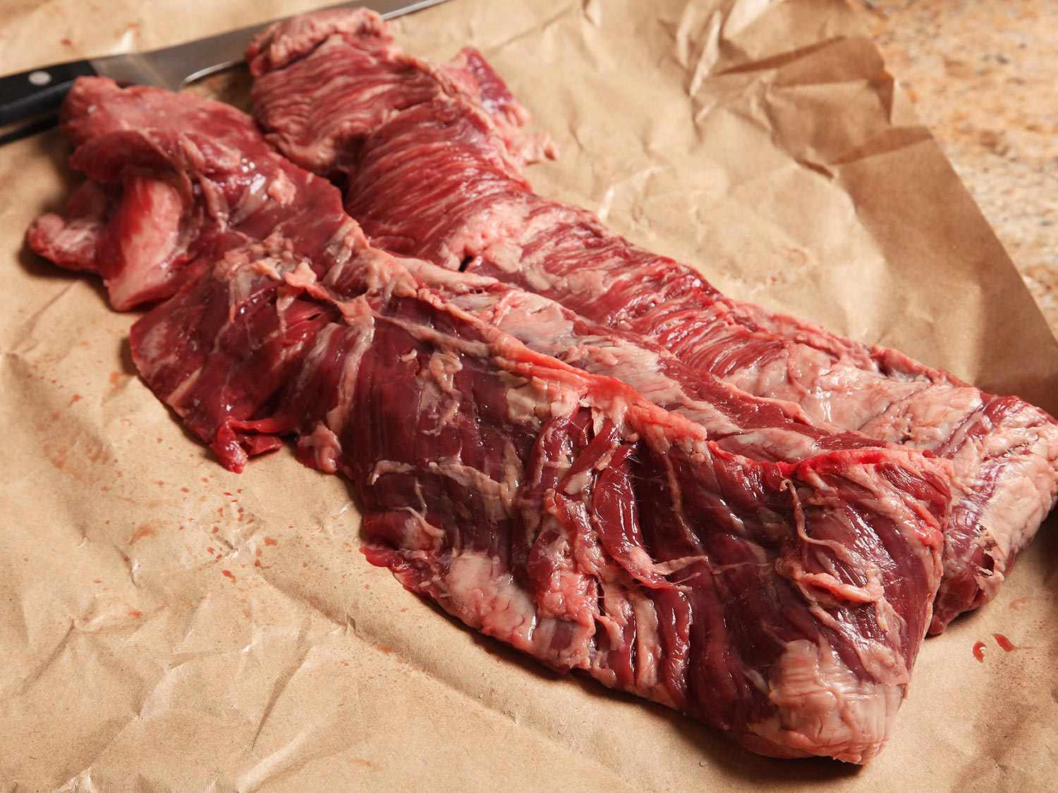 Two raw skirt steaks on butcher paper with a boning knife in the background.
