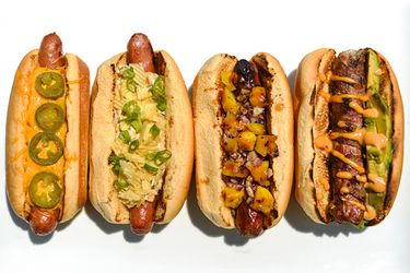 Overhead view of four hot dogs on a white surface, garnished with a variety of topping combinations.