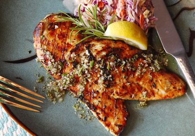 Two pieces of grilled chicken cutlet plated with lemon, rosemary and garlic