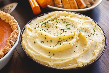 A bowl of mashed potatoes garnished with chives on a table with Thanksgiving dishes