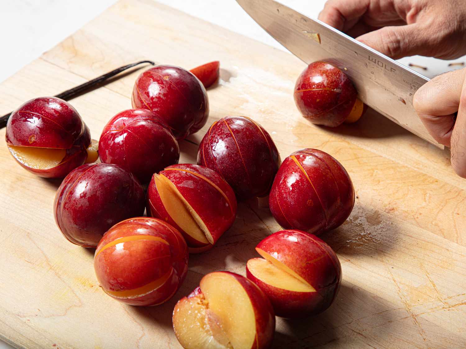 Sliced plums being prepared on a cutting board with a knife in use