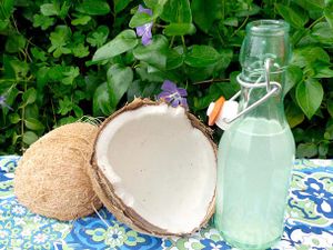 Fresh whole coconut cracked in half beside a bottle of homemade coconut rum