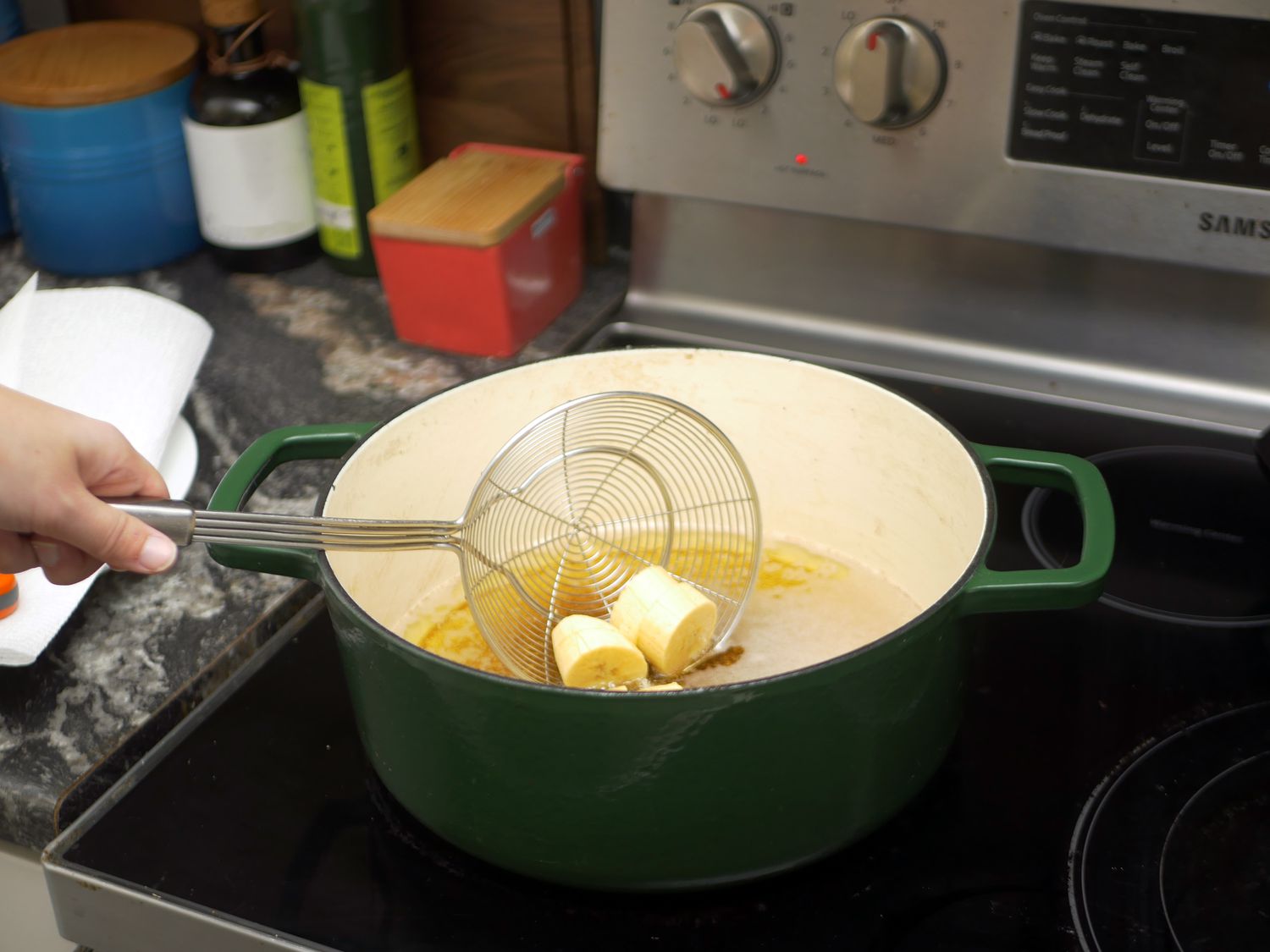 a spider strainer being used to deposit sliced plantains into hot oil in a dutch oven