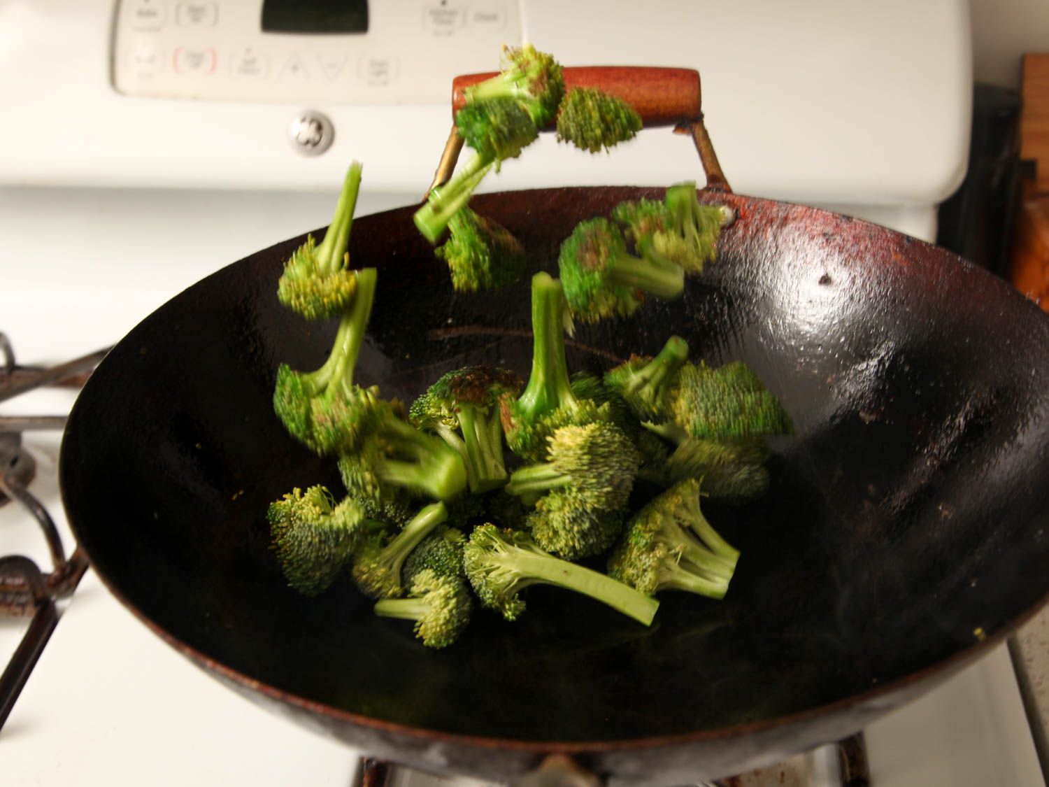 Broccoli florets being tossed and stir fried in a wok. 