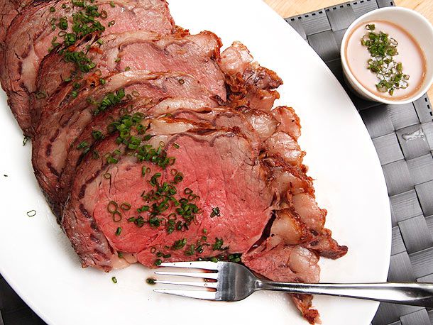 Several slices of prime rib presented on a white platter with a fork and a sauce off to the side.