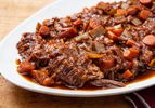 A white oval platter of Jewish-style braised brisket with onions and carrots, and jus pooling beneath the brisket.